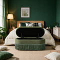 Olive green oval storage ottoman with lift-top open at the foot of a bed